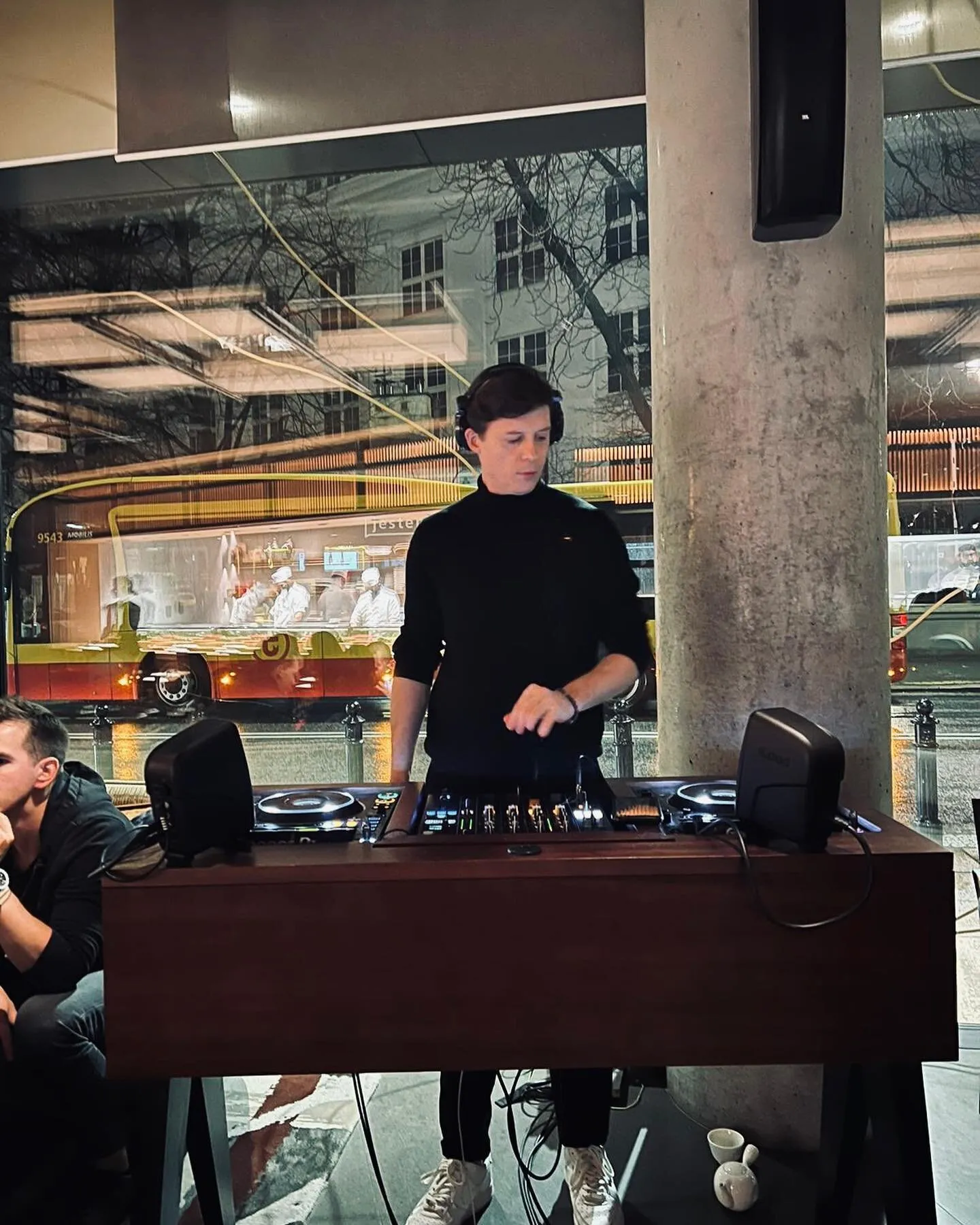 Luke Erb playing a DJ set at Nobu, Warsaw, a city tram passing the window behind him