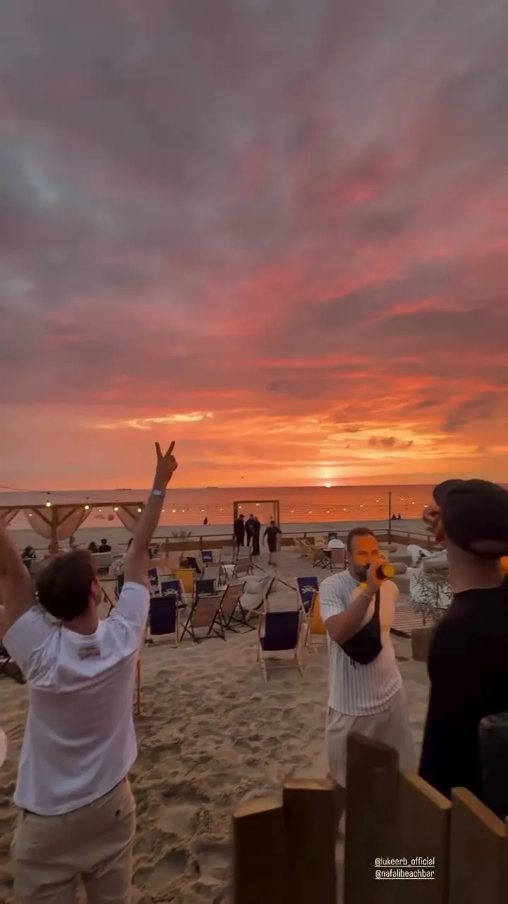 Crowd on the beach raising hands at a Luke Erb sunrise set under a pink and orange sky